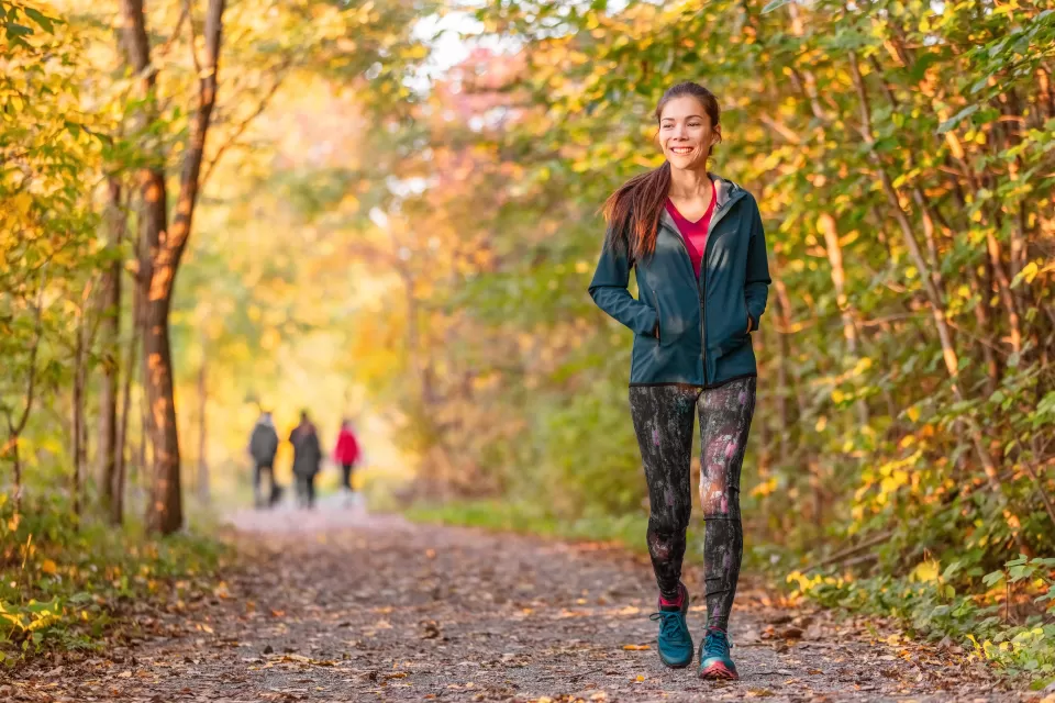 Woman in leggings and long-sleeved jacket walks in public park among fall foliage